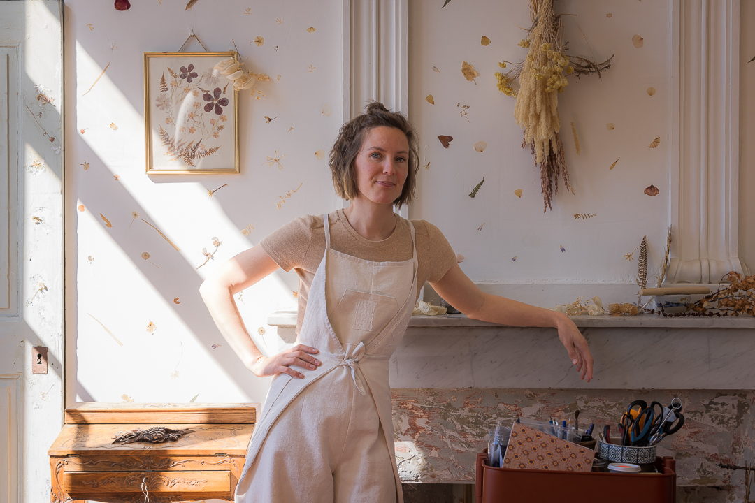 Raphaëlle se tient face à un mur décoré d'objets issu de sa pratique de la teinture naturelle, dans son atelier